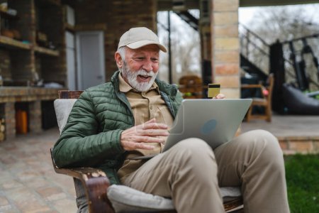 Photo for One man senior caucasian male with beard sit outdoor in day with laptop computer making online purchase shopping buy stuff hold credit card pensioner enjoy his retirement copy space real person - Royalty Free Image