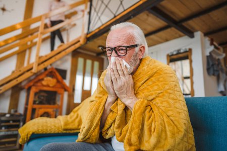 Foto de Un hombre mayor caucásico se sienta en el sofá cama en casa mantenga papel tejido resfriado común estornudos - Imagen libre de derechos