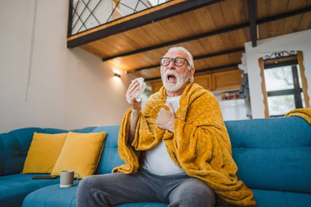 Téléchargez les photos : Un homme âgé caucasien assis sur le canapé-lit à la maison tenir papier tissu commun froid éternuer - en image libre de droit