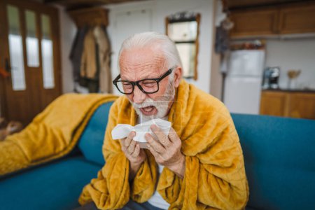 Téléchargez les photos : Un homme âgé caucasien assis sur le canapé-lit à la maison tenir papier tissu commun froid éternuer - en image libre de droit