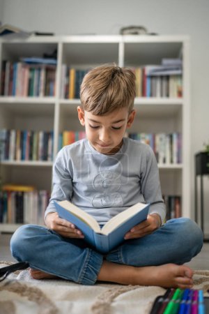 Téléchargez les photos : Caucasien garçon élève étudiant lire livre à la maison sur le plancher étude apprendre préparer pour l'école - en image libre de droit