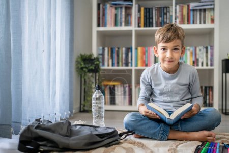 Photo for Caucasian boy pupil student read book at home on the floor study learn prepare for school - Royalty Free Image