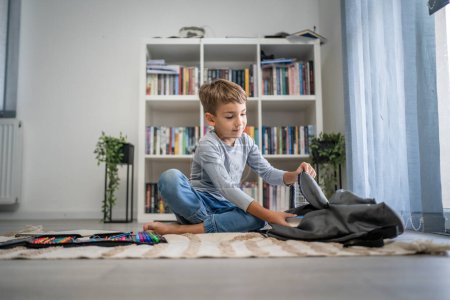 Photo for Small caucasian boy pupil child prepare his backpack for first day of school back to school and education concept sit on the floor at home packing his stuff real people copy space - Royalty Free Image