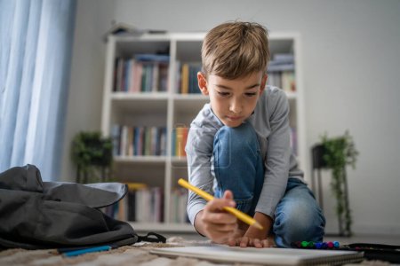 Téléchargez les photos : Un écolier Petit garçon caucasien jouer à la maison dessiner sur le sol faire des devoirs développement de l'enfance grandir et l'éducation concept copier espace vie domestique - en image libre de droit