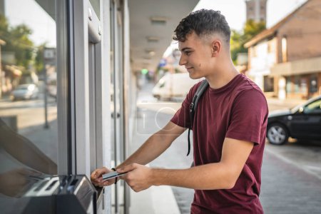 man teenage student using credit card and withdrawing cash at the ATM