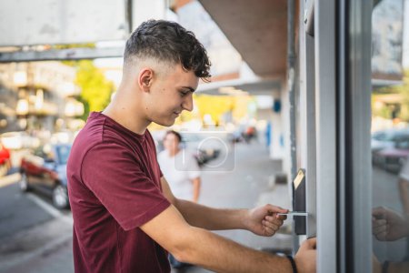 Téléchargez les photos : Homme adolescent étudiant en utilisant la carte de crédit et retirer de l'argent au guichet automatique - en image libre de droit