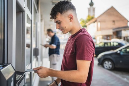 Foto de Estudiante adolescente hombre usando tarjeta de crédito y retirar dinero en efectivo en el cajero automático - Imagen libre de derechos