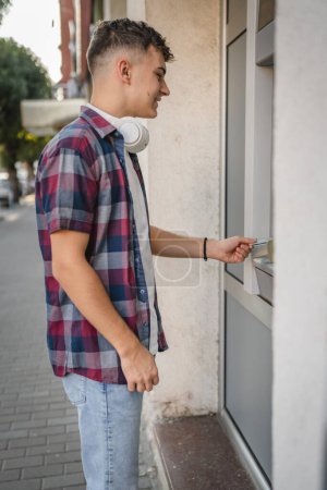 Foto de Estudiante adolescente hombre usando tarjeta de crédito y retirar dinero en efectivo en el cajero automático - Imagen libre de derechos