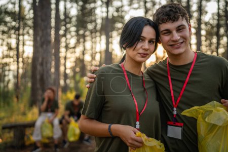 Téléchargez les photos : Portrait couple en face de groupe d'amis bénévoles se préparent à recueillir les déchets et la nature propre forêt dans la journée d'été au ralenti - en image libre de droit