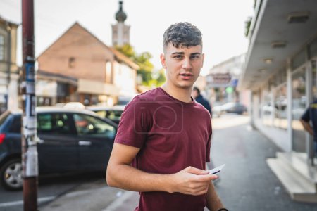 Téléchargez les photos : Portrait de l'homme adolescent debout devant la banque ATM détenir carte de crédit - en image libre de droit