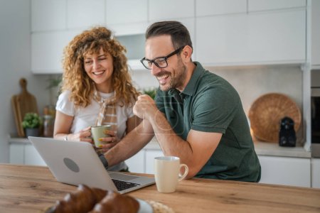 Photo for Happy couple caucasian adult man and woman husband and wife morning routine use laptop computer during breakfast at home bright photo copy space - Royalty Free Image