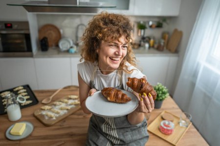 Foto de Una mujer caucásica adulta de pie en la cocina con croissant fresco para el desayuno todos los días por la mañana - Imagen libre de derechos