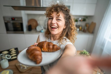 Téléchargez les photos : Une femme caucasienne adulte se tient dans la cuisine avec croissant frais pour le petit déjeuner routine quotidienne du matin - en image libre de droit