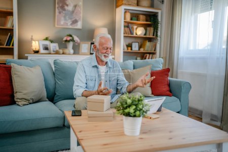 Photo for One senior man grandfather pensioner with gray hair and beard receive presents in box open read card happy smile in front of laptop computer at home having online video call copy space - Royalty Free Image