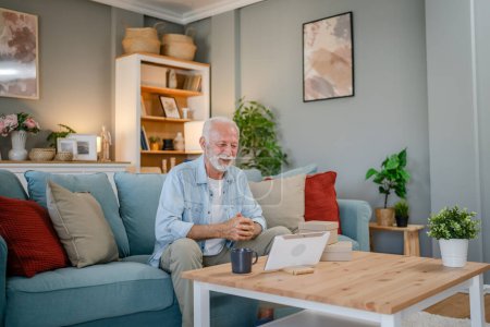 Téléchargez les photos : Un homme âgé grand-père pensionné avec les cheveux gris et la barbe recevoir des cadeaux dans la boîte ouverte carte de lecture heureux sourire devant ordinateur portable à la maison ayant en ligne espace de copie d'appel vidéo - en image libre de droit