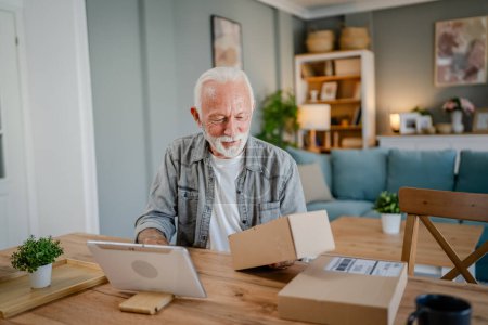 Photo for One senior caucasian man at home hold cardbox package delivered gift or order use digital tablet online to check shipment shopping status or for video call copy space - Royalty Free Image