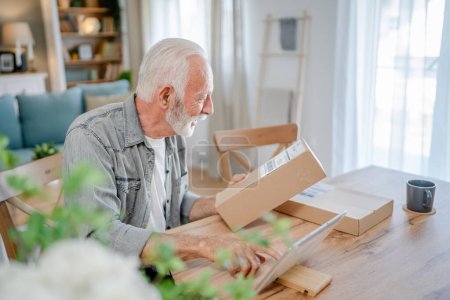 Téléchargez les photos : Un homme caucasien senior à la maison tenir paquet cardbox livré cadeau ou une commande - en image libre de droit