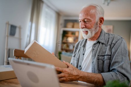 Téléchargez les photos : Un homme caucasien senior à la maison tenir paquet cardbox livré cadeau ou une commande - en image libre de droit