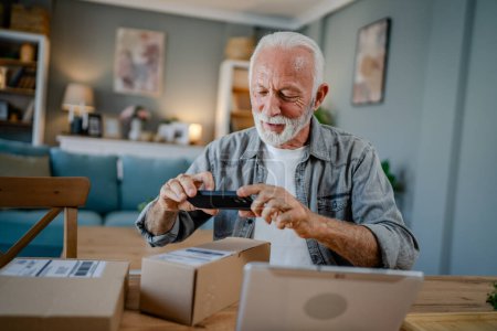 Photo for One senior caucasian man at home hold cardbox package delivered gift or order use mobile phone smartphone online to check shipment shopping status scan code or for video call copy space - Royalty Free Image