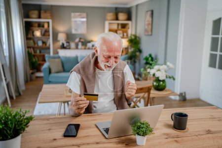 Photo for One man senior caucasian male grandfather sit at home use credit card and laptop computer shopping online use internet for online purchase active modern senior - Royalty Free Image
