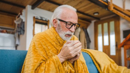 Foto de Un hombre mayor caucásico se sienta en el sofá cama en casa sostenga la taza de té resfriado común estornudos enfermos atrapados frío - Imagen libre de derechos