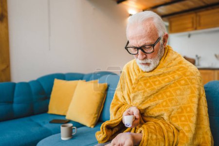 Téléchargez les photos : Un homme âgé caucasien assis sur le canapé-lit à la maison tenir thermomètre vérifier la température du corps fièvre ou rhume éternuer malade attrapé froid - en image libre de droit