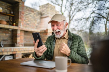 Photo for One man senior caucasian male with gray beard and cap sit outdoor in spring or autumn day happy smile use mobile smart phone for video call copy space real people - Royalty Free Image