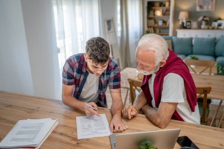 Photo for One student teenage caucasian man teen study learn with help of his tutor professor or grandfather senior man at home having private lesson to prepare for exam education concept real people copy space - Royalty Free Image