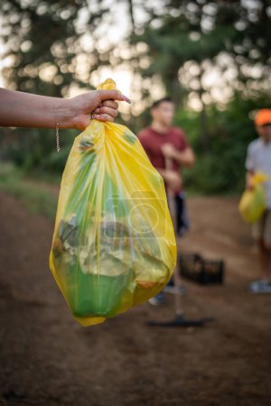 Foto de Manos de una persona caucásica desconocida sostienen bolsa recogiendo basura botellas de plástico y papel del bosque limpiando la naturaleza en el concepto de ecología de cuidado ambiental de día soleado - Imagen libre de derechos