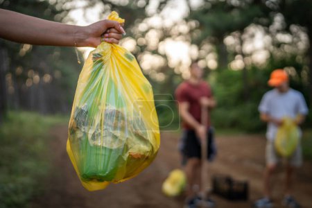 Photo for Hands of unknown caucasian person hold bag picking up waste garbage plastic bottles and paper from the forest cleaning up nature in sunny day environmental care ecology concept - Royalty Free Image