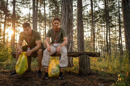 Téléchargez les photos : Couple ou adolescent amis génération Z mâle et femme caucasien homme femme ramasser déchets déchets bouteilles en plastique et du papier de la forêt nettoyage de la nature dans ensoleillé jour écologie soins concept - en image libre de droit