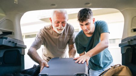 Photo for Two men Teenager and senior man grandfather grandson pack baggage luggage in trunk of the car prepare for road-trip vacation or student go to campus - Royalty Free Image