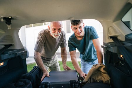 Téléchargez les photos : Deux hommes adolescent et senior homme grand-père petit-fils sac bagages bagages dans le coffre de la voiture se préparent pour les vacances sur la route ou étudiant aller sur le campus - en image libre de droit