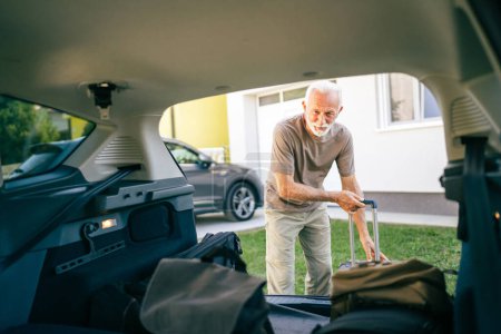 Photo for One senior man travel concept male take stuff belongings from the back or put suitcase in trunk of the car while moving to travel or arrive to destination real people copy space - Royalty Free Image