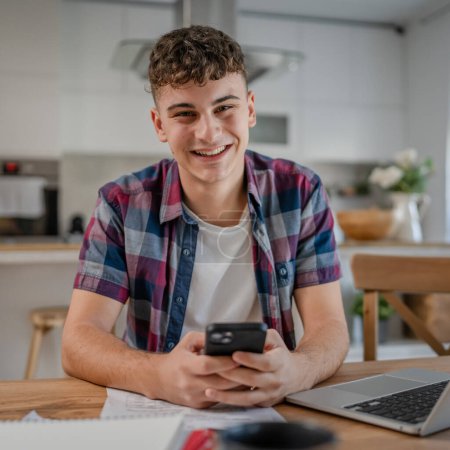 Téléchargez les photos : Jeune homme caucasien adolescent étudiant étudier à la maison utiliser téléphone mobile smartphone textos sms - en image libre de droit