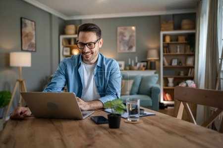 Téléchargez les photos : Un homme adulte caucasien mâle avec barbe travail sur son ordinateur portable à la maison heureux sourire succès entrepreneur indépendant ou concept de travail à distance - en image libre de droit