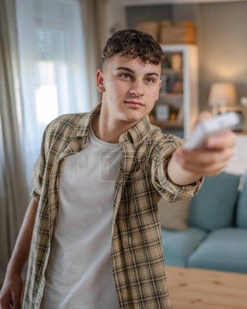 Téléchargez les photos : Jeune homme adolescent caucasien utiliser la télécommande pour la télévision ou la climatisation - en image libre de droit