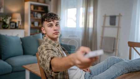 Téléchargez les photos : Jeune homme adolescent caucasien utiliser la télécommande pour la télévision ou la climatisation - en image libre de droit