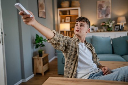 Photo for Young caucasian teenage man use remote control for TV or air-condition - Royalty Free Image
