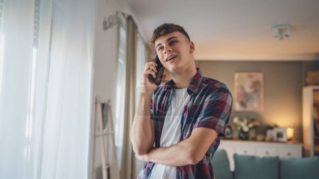 Téléchargez les photos : Un homme caucasien adolescent garçon utilise smartphone téléphone mobile pour faire un appel parler à la maison sourire heureux - en image libre de droit