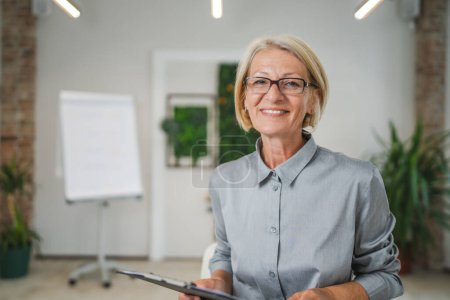 Photo for Portrait of one mature blonde caucasian woman with eyeglasses in the office at work happy smile looking to the camera confident copy space - Royalty Free Image