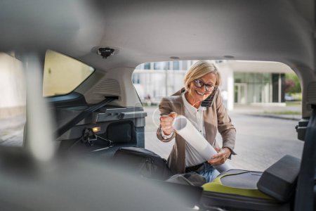Photo for One mature blonde beautiful business woman travel concept female take stuff belongings from the back of her car while moving or arrive to destination or work make a phone call real people copy space - Royalty Free Image