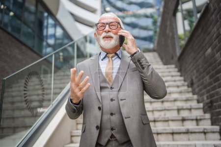 Photo for Portrait of senior man with beard businessman in suit stand outdoor in front of modern building corporation use mobile phone smartphone make a call talk real person copy space - Royalty Free Image