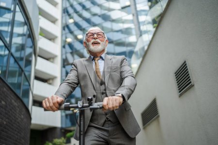 Téléchargez les photos : Un homme caucasien senior debout sur scooter électrique coup de pied conduite dans la ville e-scooter mode de transport respectueux de l'environnement personnes réelles costume homme d'affaires devant l'espace de copie de l'entreprise - en image libre de droit