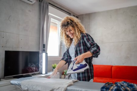 Foto de Mujer adulta caucásica mujer feliz usando plancha eléctrica para planchar ropa en casa tareas domésticas concepto de tareas domésticas personas reales espacio de copia de trabajo doméstico - Imagen libre de derechos
