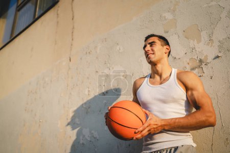 Photo for One young caucasian man male athlete stand outdoor hold basketball ball wear white tank top a-shirt strong muscular real person copy space happy smile confident healthy lifestyle concept - Royalty Free Image