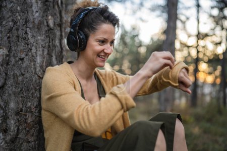 Photo for One woman young adult caucasian female sit alone in the park or forest in nature with headphones preparing for guided meditation self-care manifestation practice mental emotional balance concept - Royalty Free Image
