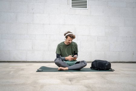 Téléchargez les photos : Un homme jeune homme caucasien adulte se préparer à la formation guidée yoga ou méditation tenir tablette numérique tout en étant assis à l'extérieur avec casque pratique d'auto-soins de bien-être concept d'équilibre de paix intérieure - en image libre de droit