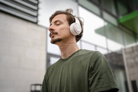 Photo for One man young adult caucasian male eyes closed for guided training yoga or meditation while sitting outdoor with headphones self-care practice real people well-being inner peace and balance concept - Royalty Free Image