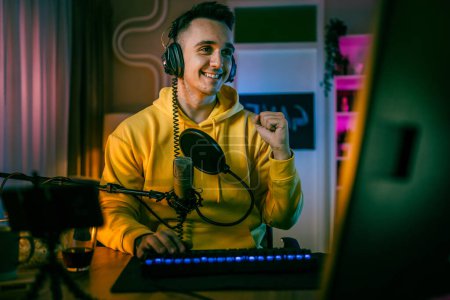 Photo for Young man play video games on pc computer while streaming to social media or internet online playtrough or walktrough video male gamer having fun at home wear headphone happy winning copy space - Royalty Free Image